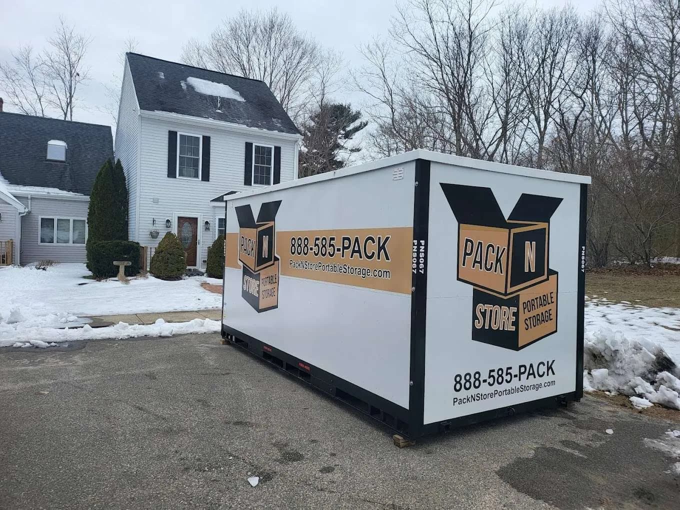 A container on a plowed driveway with snowbanks either side, planks under both corners.