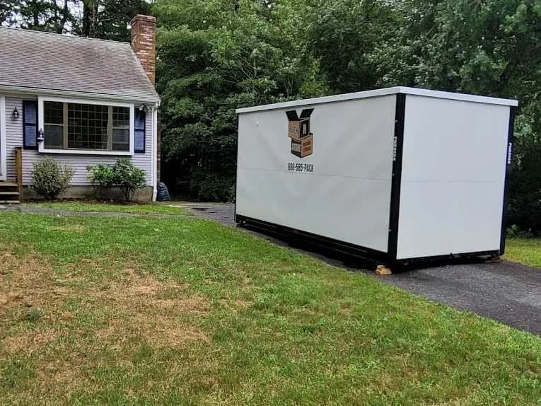 A container spanning the edge of a driveway onto the lawn, doors facing the house.