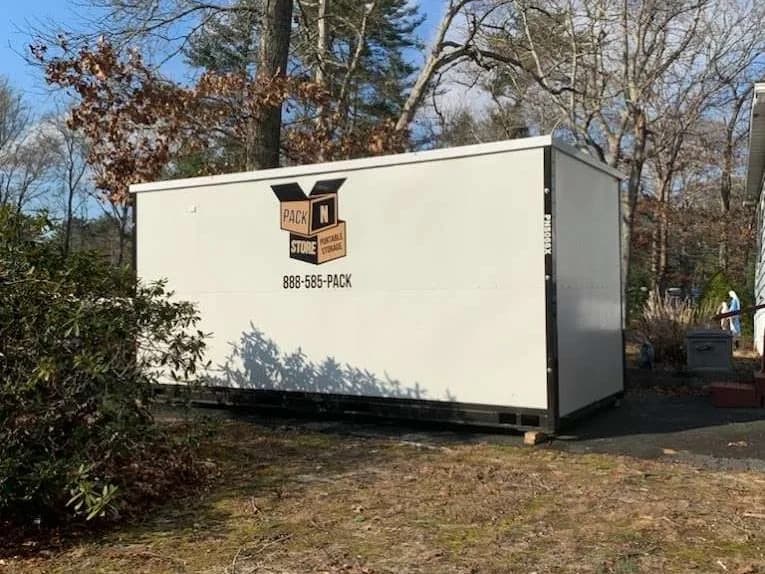 A container on packed ground at the edge of a drive, bare oaks behind.