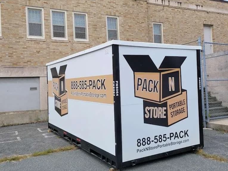 A container in a paved lot beside a brick institutional building.