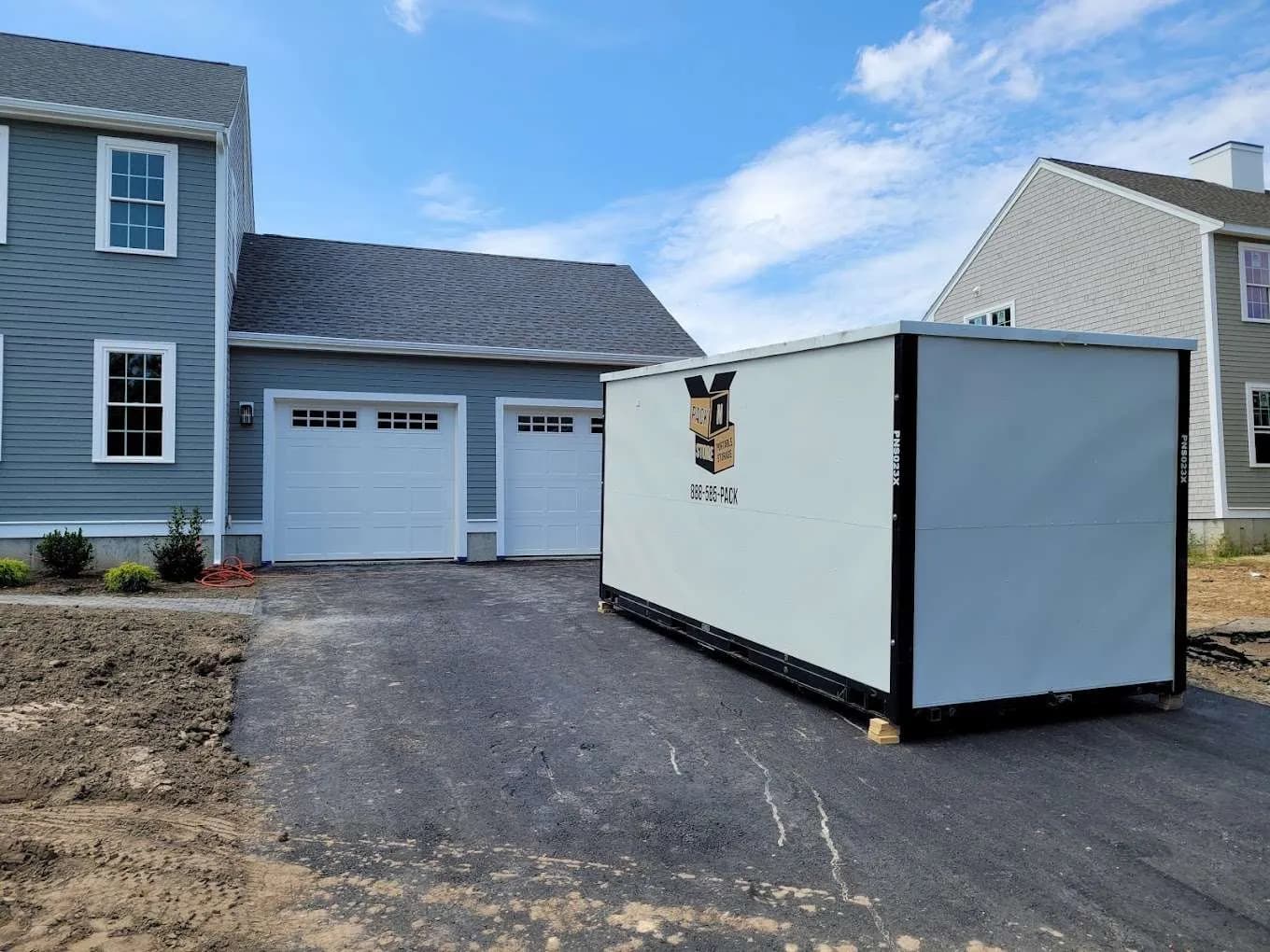 A container on a fresh driveway at a newly built house, grading not yet finished.
