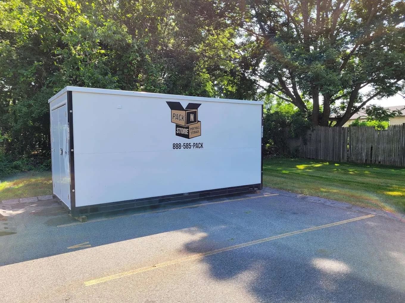 A container placed across parking spaces against a fence line, doors on the open end.