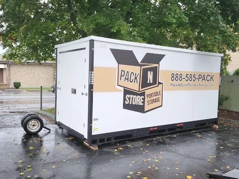 A container just set down on wet pavement, the delivery trailer's wheel still in frame.