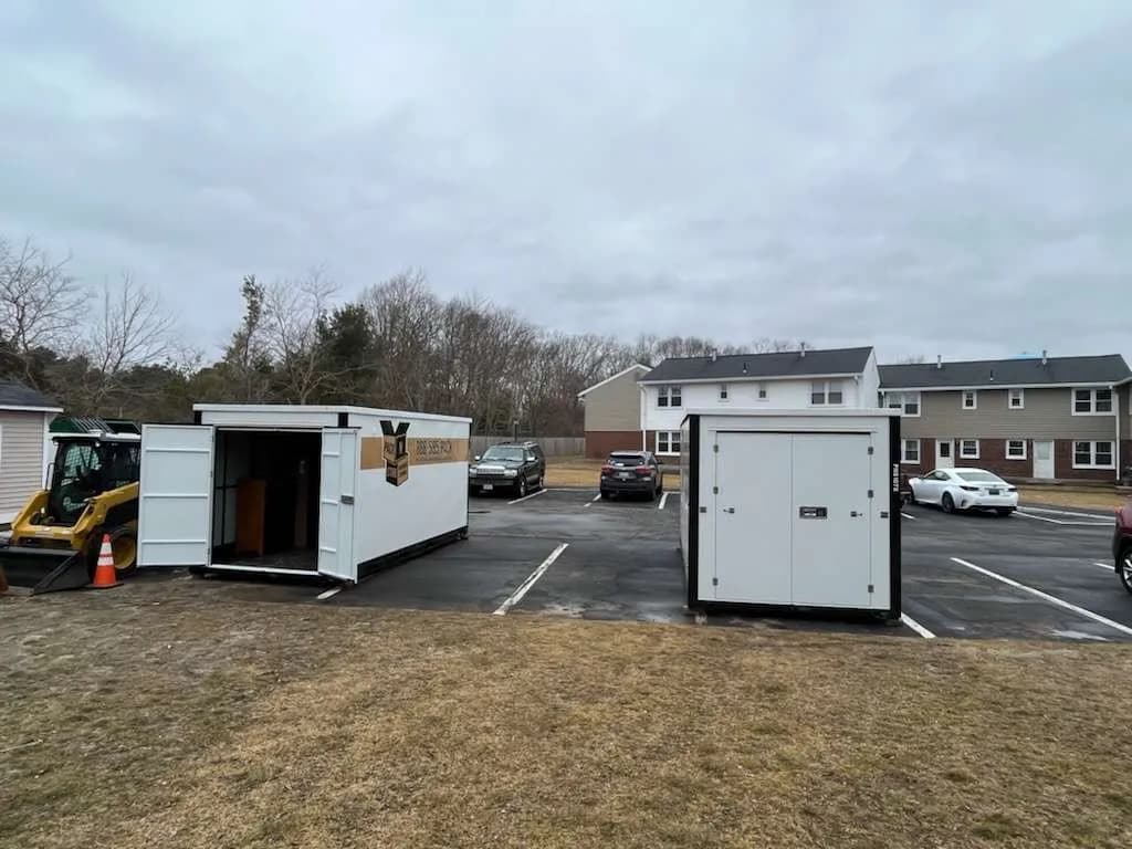 Two containers in a parking lot beside a skid steer, one with its doors open.