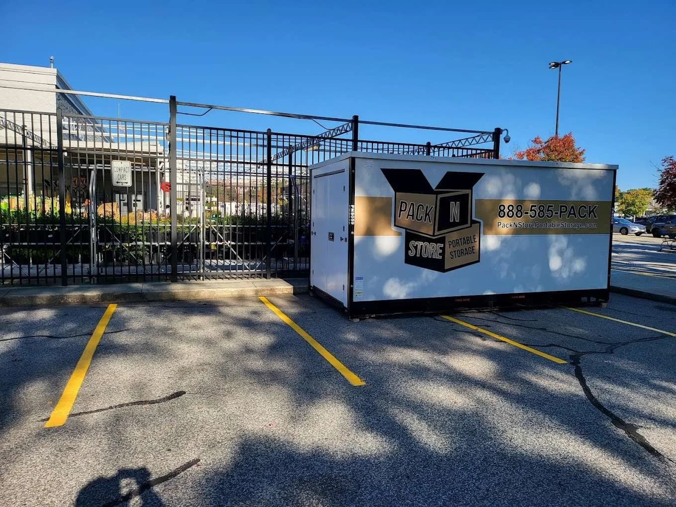 A container in a retail parking lot beside a fenced garden centre.