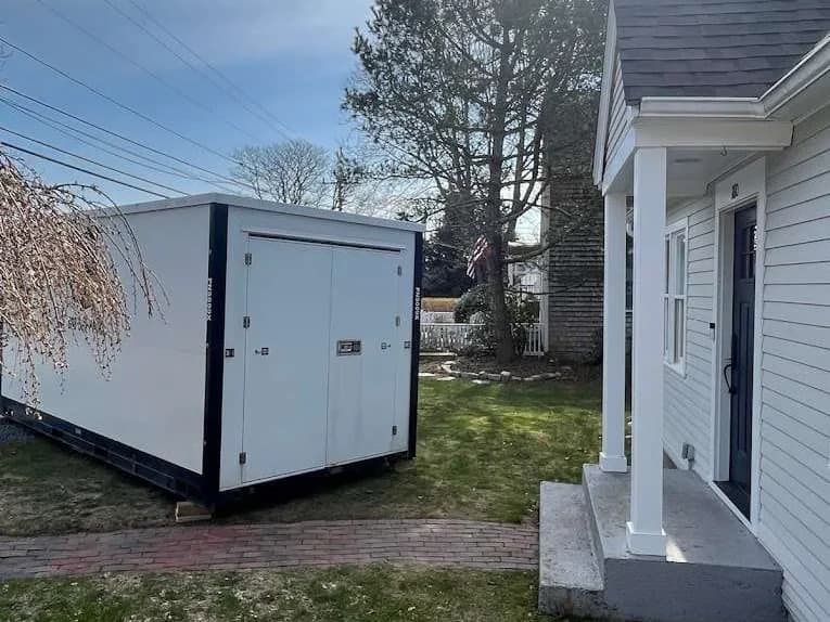 A container on a lawn beside a brick walkway, set back from the house.