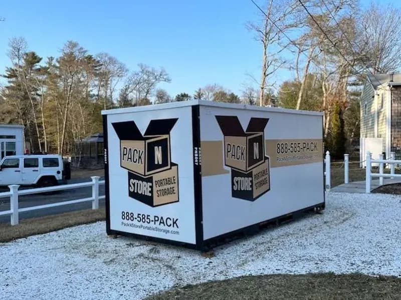 Branded Pack N Store container on a gravel pad beside a home